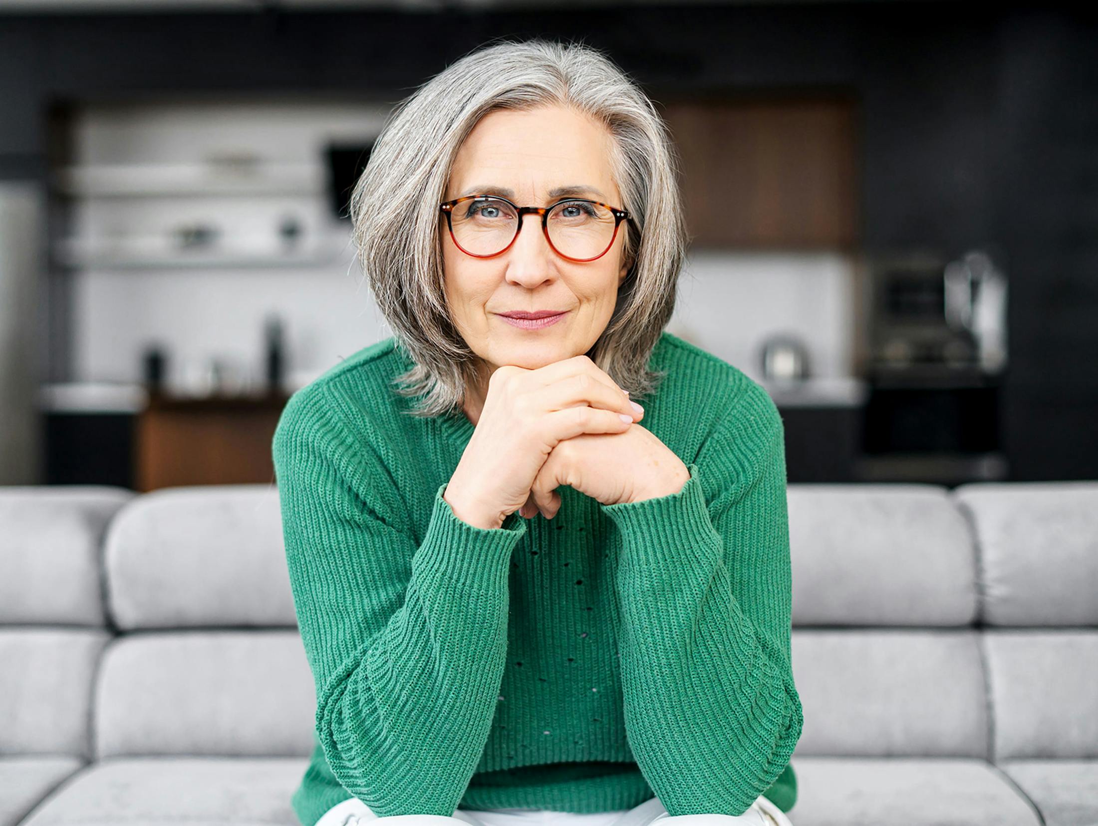 Older woman sitting on couch with her hands under her chin