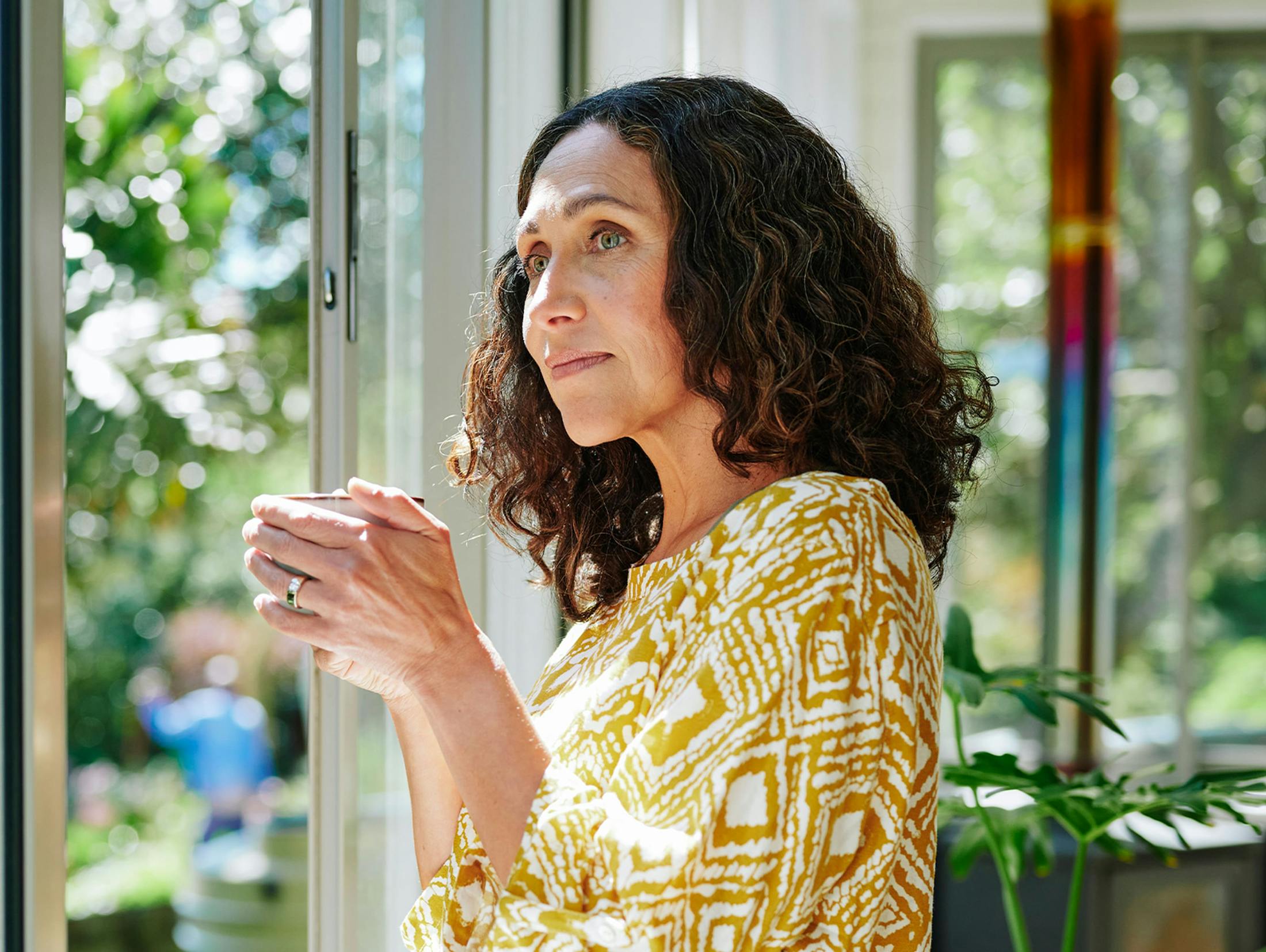 woman looking out the window while holding a mug