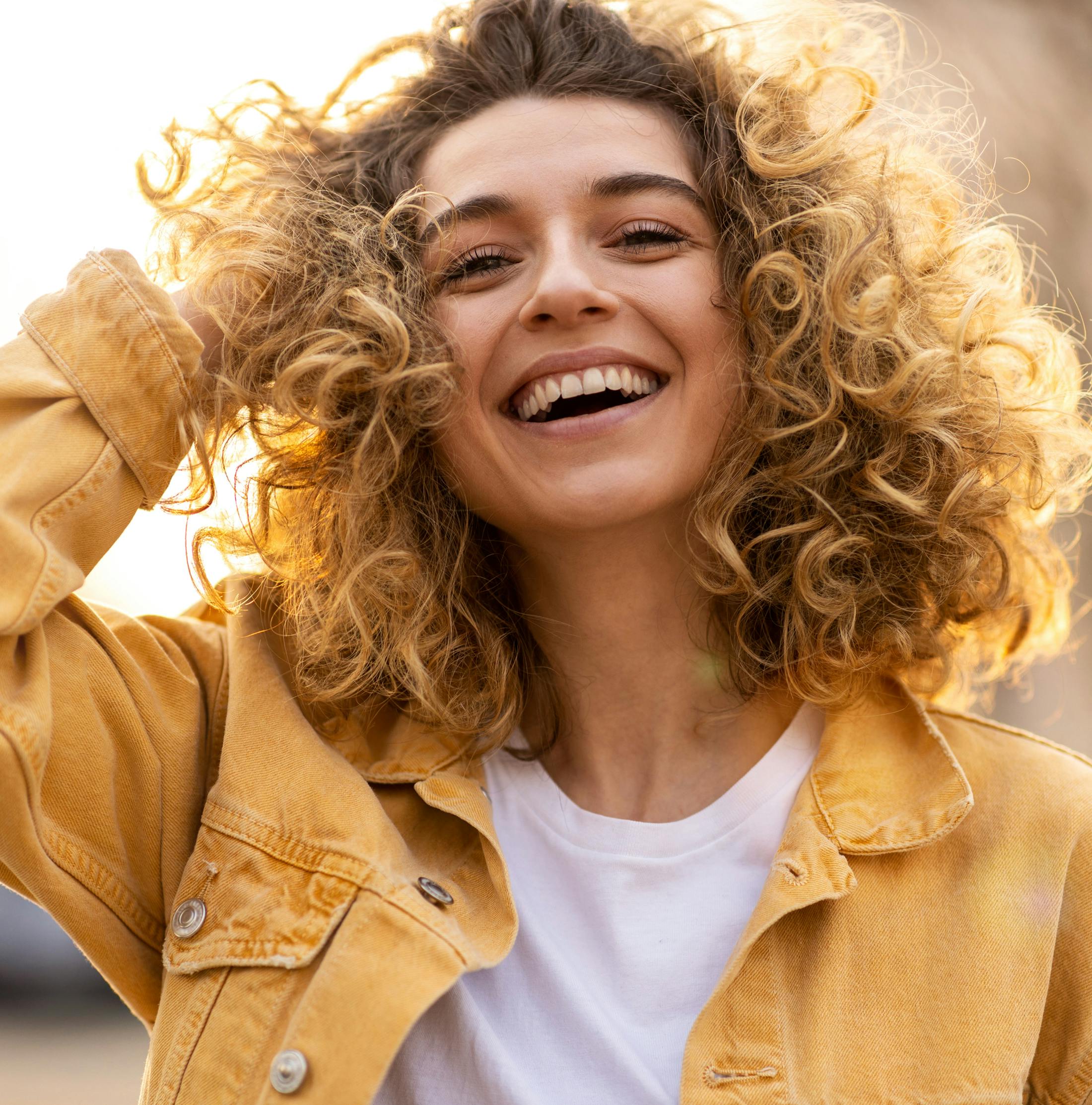 woman with curly hair smiling in yellow jacket