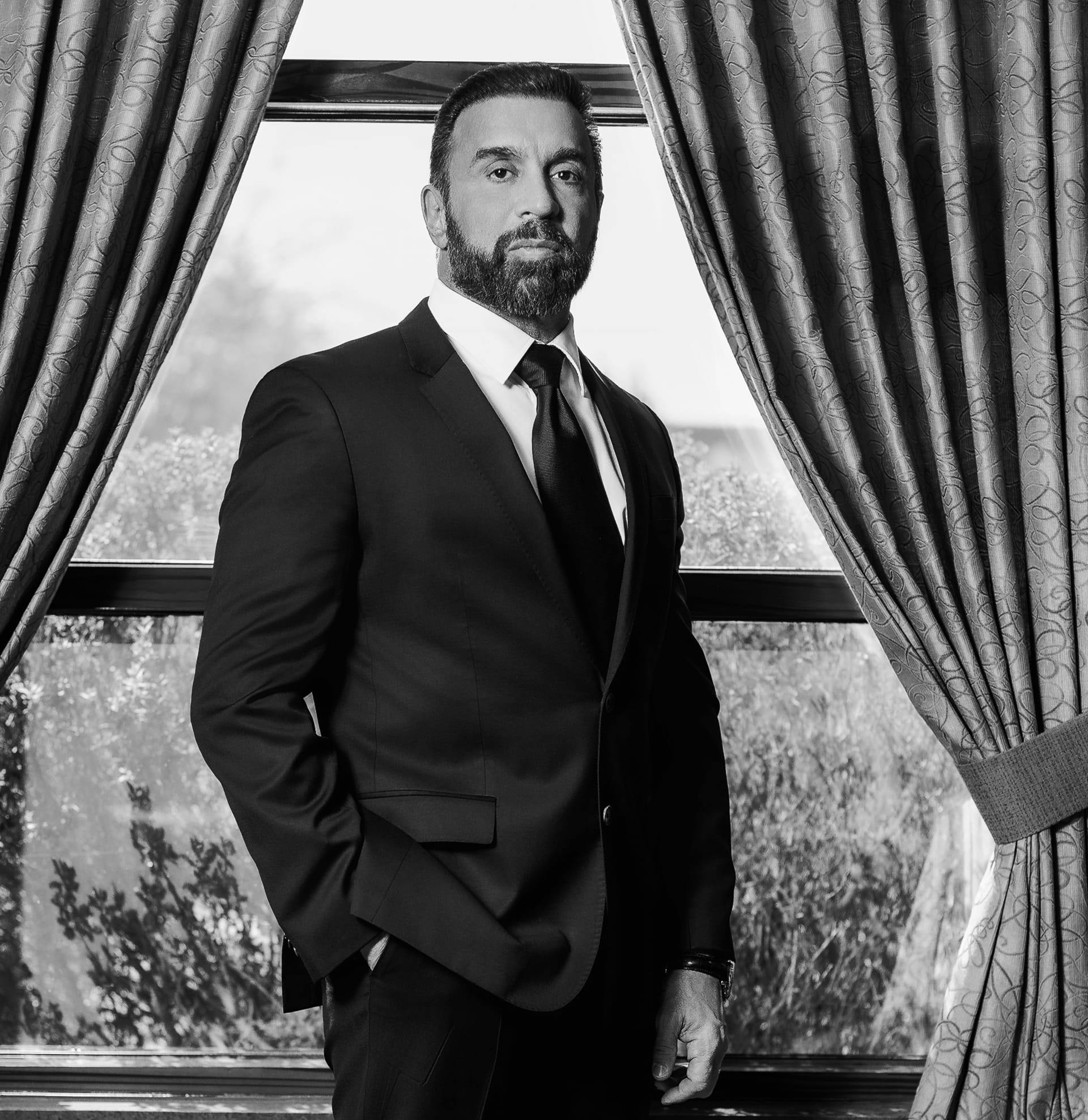 Dr. Frank Stile in black-and-white wearing a suit with curtains in the background