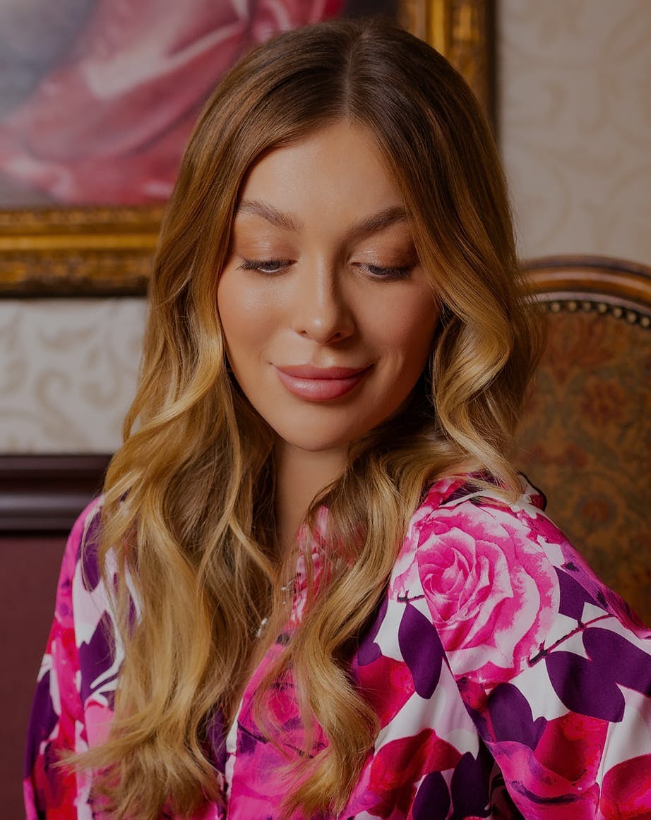 Woman with long blonde hair and floral top smiling slightly, indoors