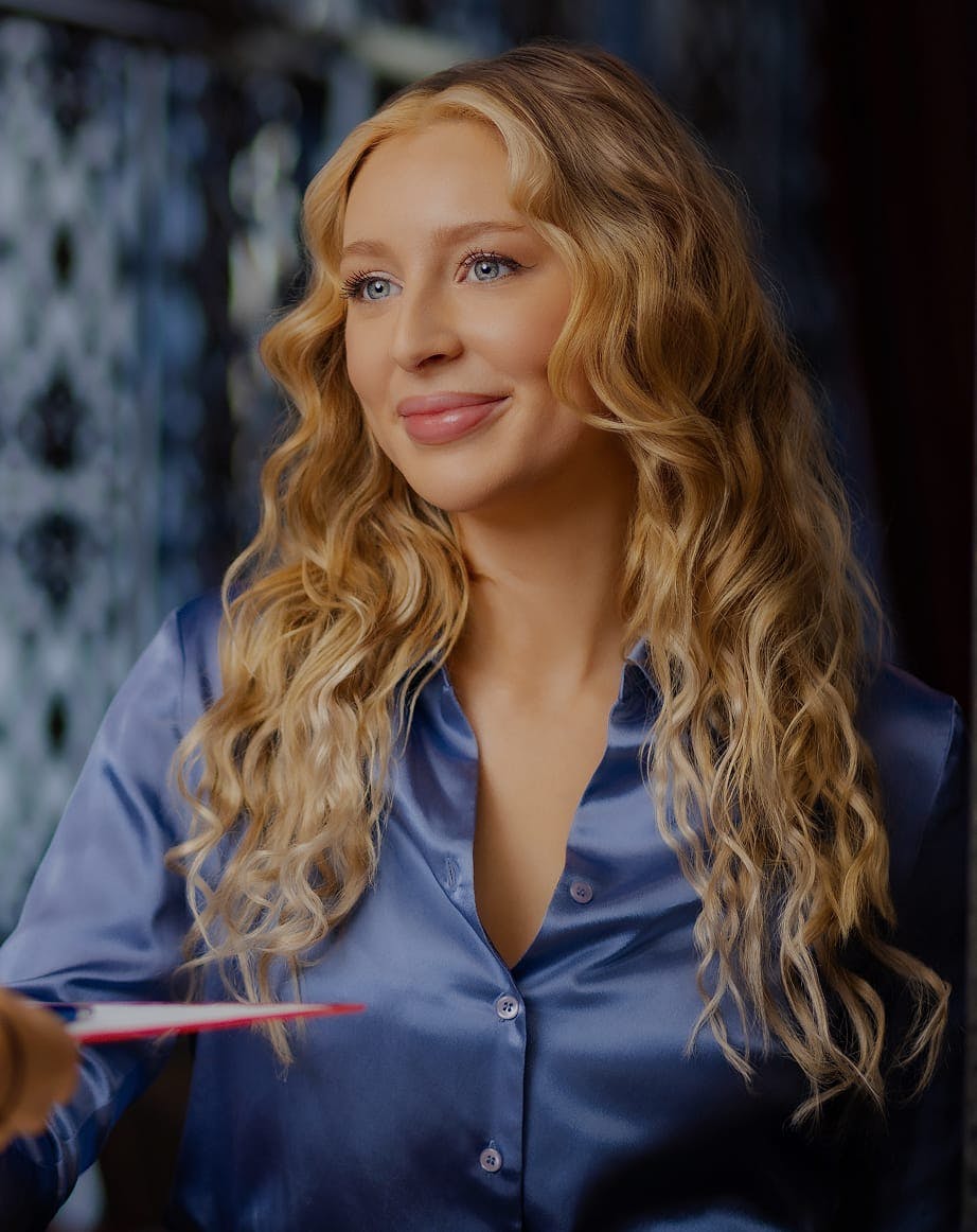 Smiling woman with wavy blonde hair, seated in front of a blue backdrop