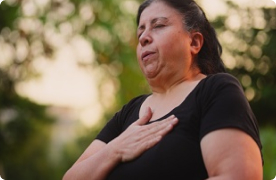 Una mujer está afuera con la mano en el corazón. Tiene los ojos cerrados y respira para calmarse.