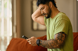 Un hombre con tatuajes en el brazo marca un número en un teléfono inteligente.