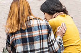 Una foto de dos amigas, tomada desde atrás. Están hablando y una amiga le pone la mano en la espalda a la otra.