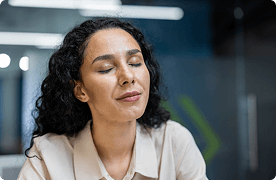 Una mujer con traje de negocios se toma un momento para cerrar los ojos y centrarse.
