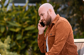 Un hombre con la cabeza rapada habla por teléfono afuera.