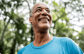 Un hombre mayor sonríe mientras camina bajo los árboles.