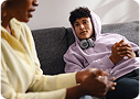 Una madre y su hijo adolescente platicando en el sofá.