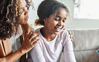 Una madre pone las manos sobre los hombros de su hija pequeña.