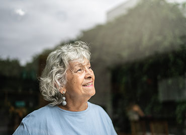 An older woman looks out her window.