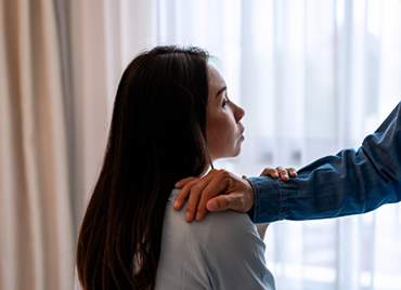 Someone places a hand on a woman's shoulder in comfort.