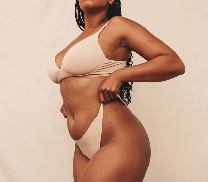 woman in underwear and bra lifting up her underwear to her waist