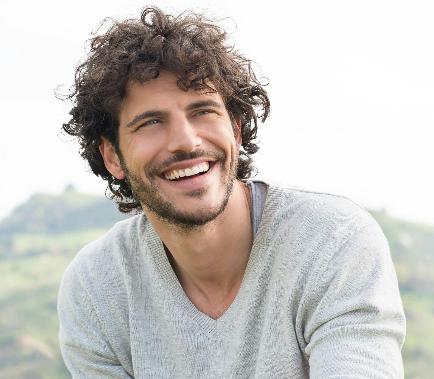 man with curly hair outside smiling