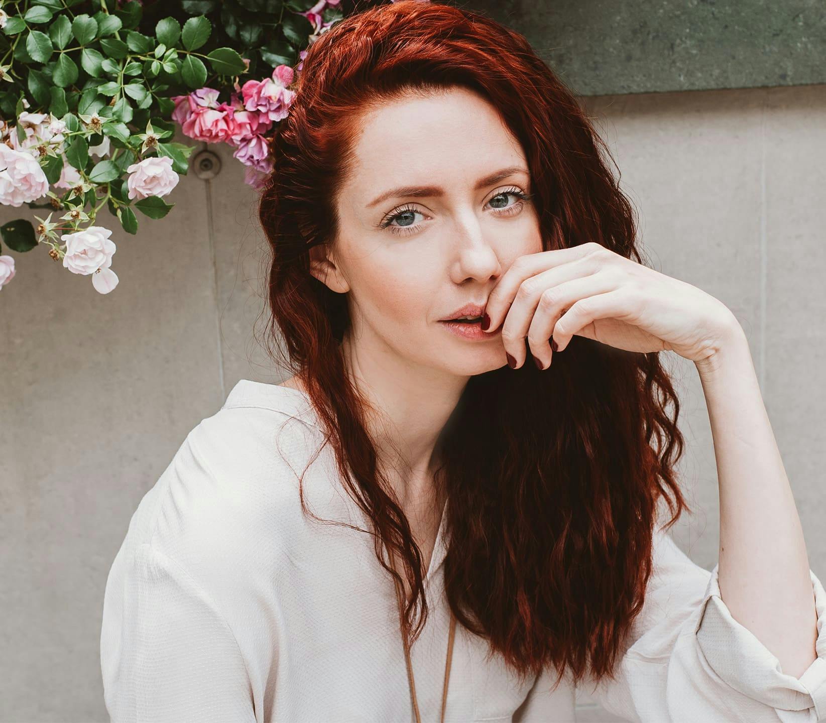 woman with dark red hair and her hand near her mouth