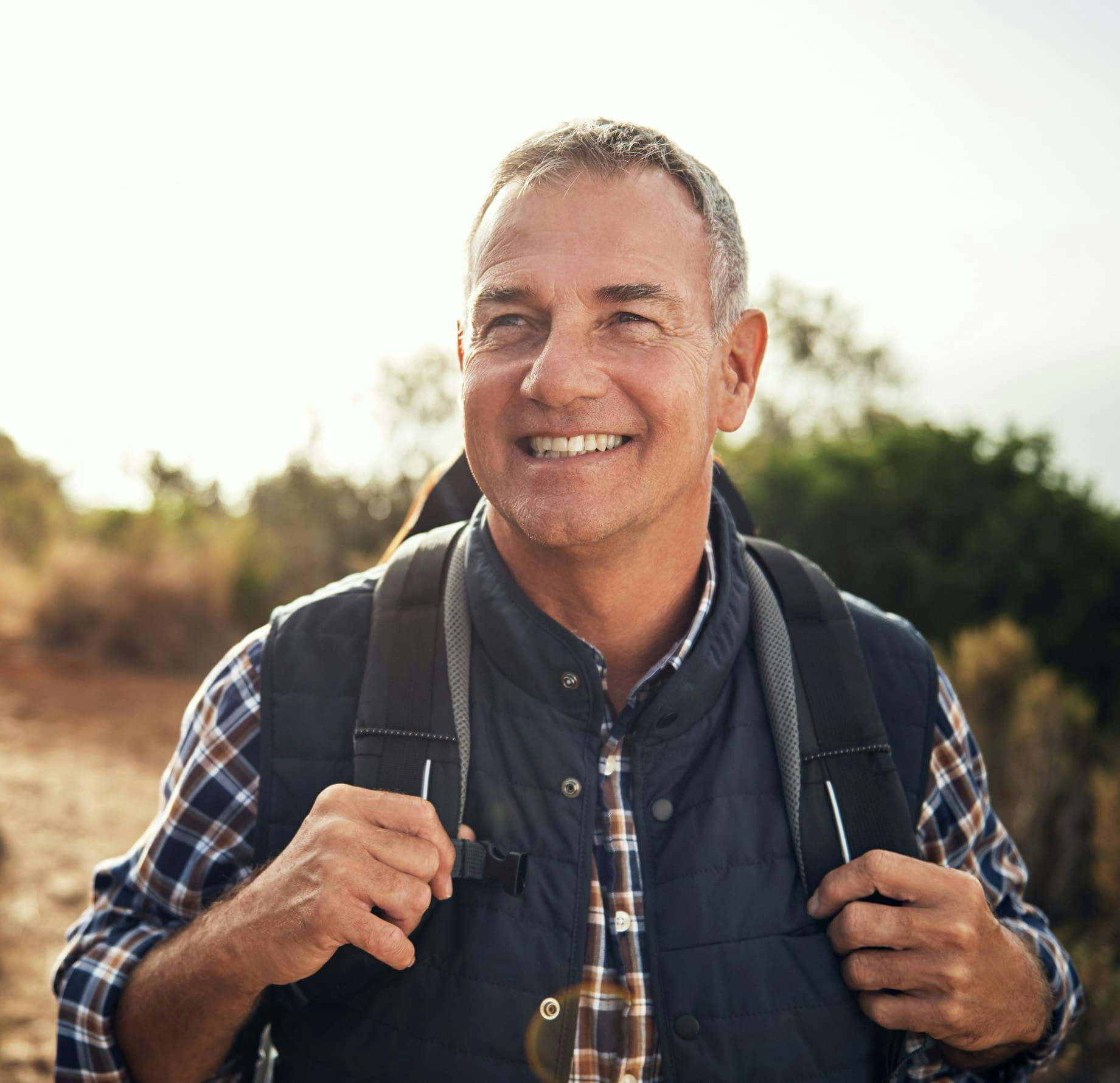 man hiking outside with hands holding backpack straps