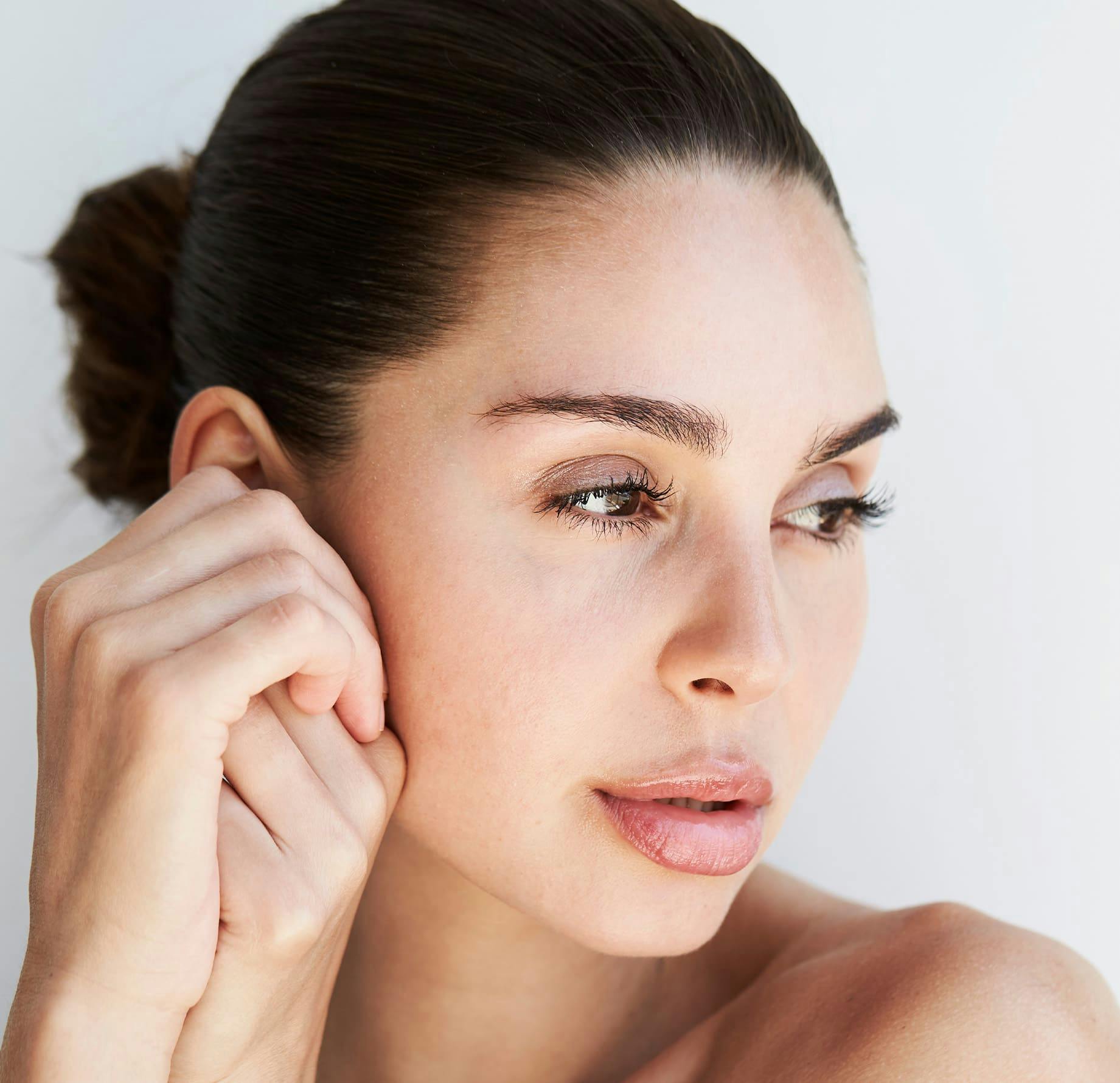 woman with her hair tied up while she touches her ear