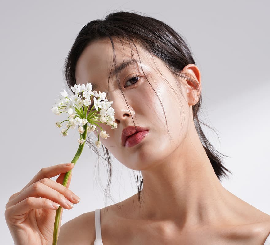 asian woman holding a flower infront of her eye