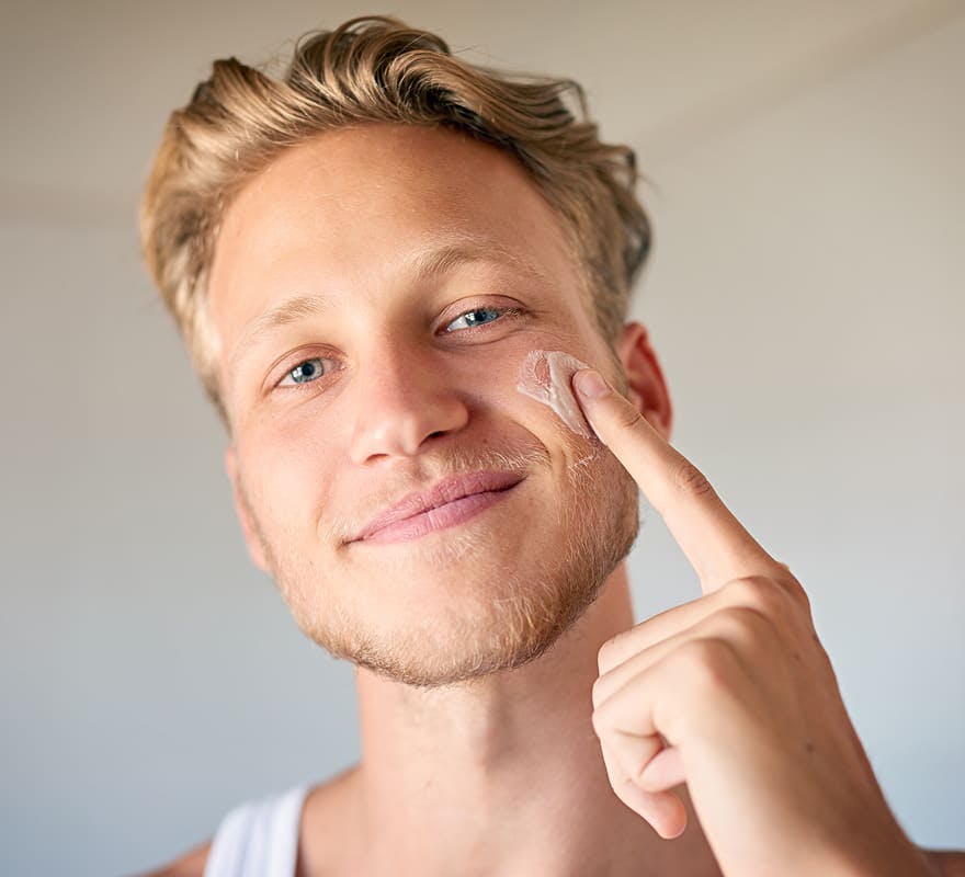 man smiling and putting skincare on his cheek