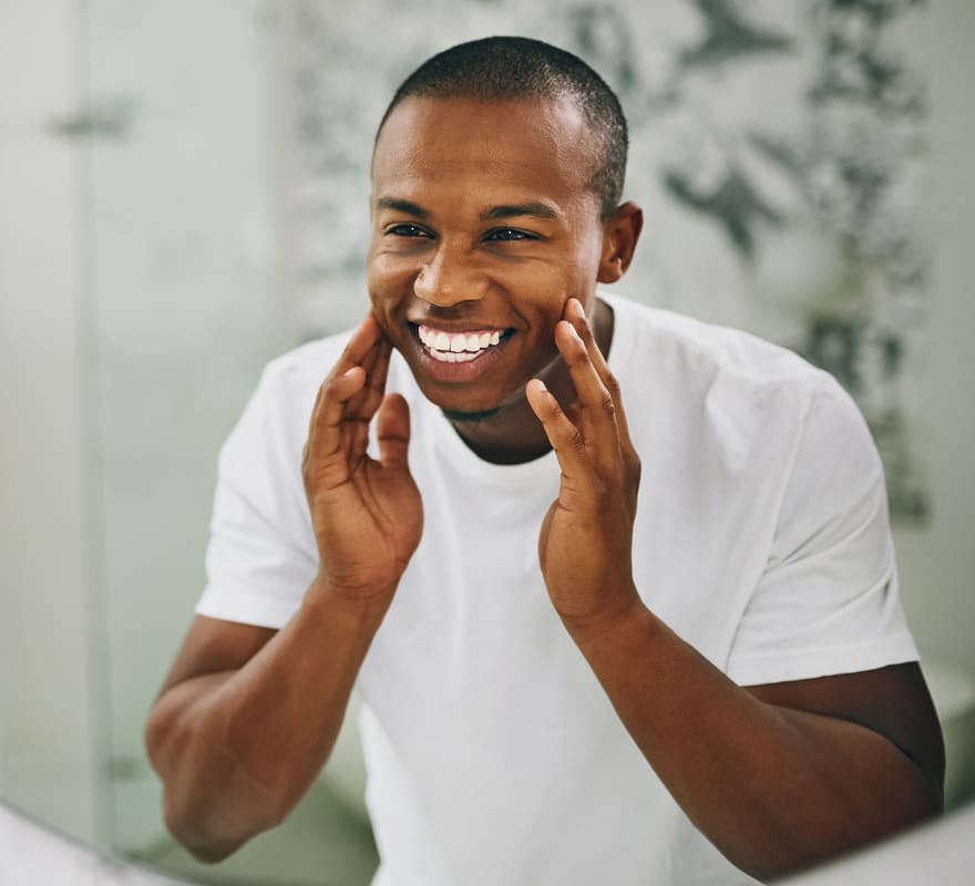 man smiling in mirror and touching his cheeks