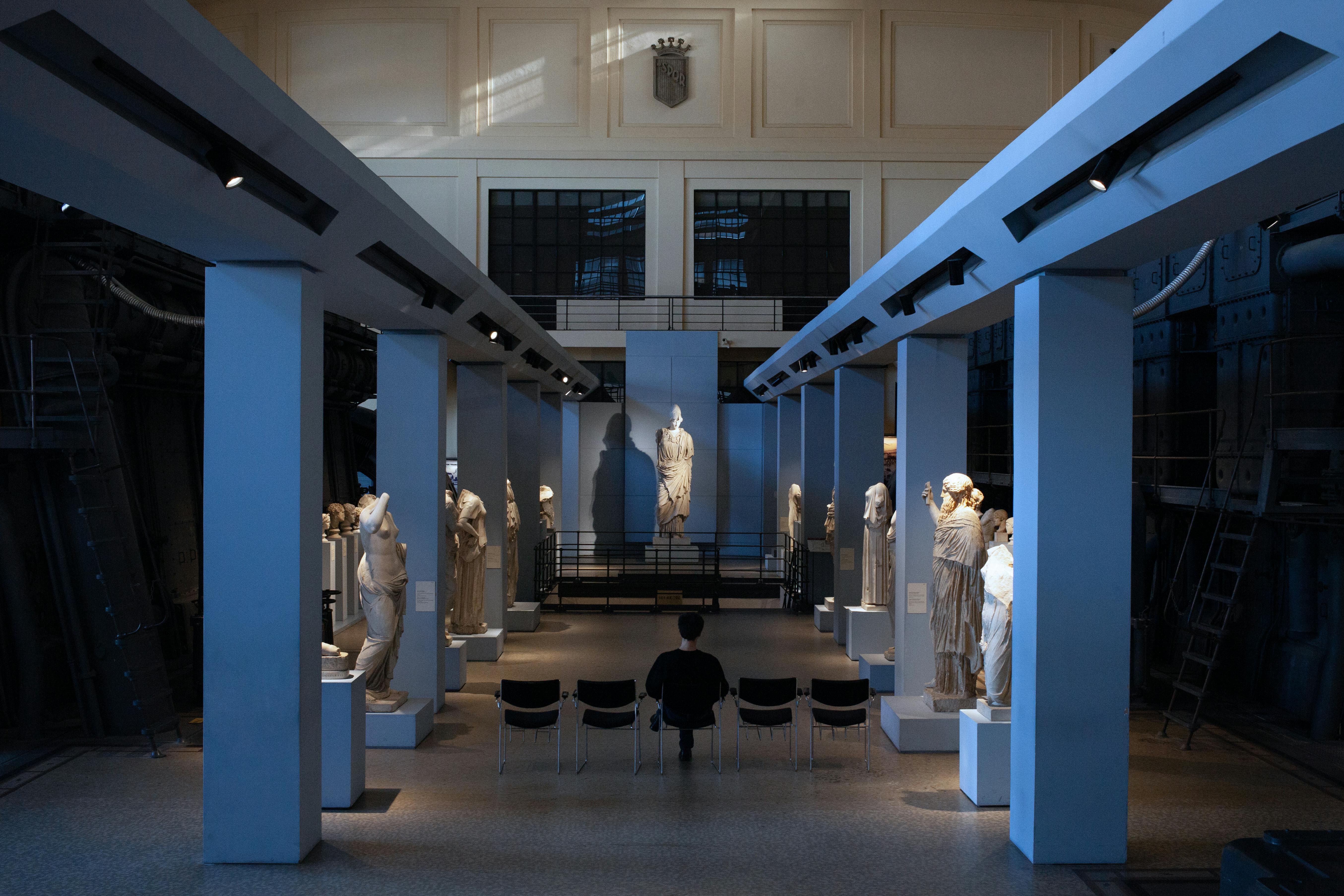 Roma, Museo Centrale Montemartini, Sala Macchine. Copie di statue greche ai lati e una scultura di Atena sul fondo e visitatore seduto.