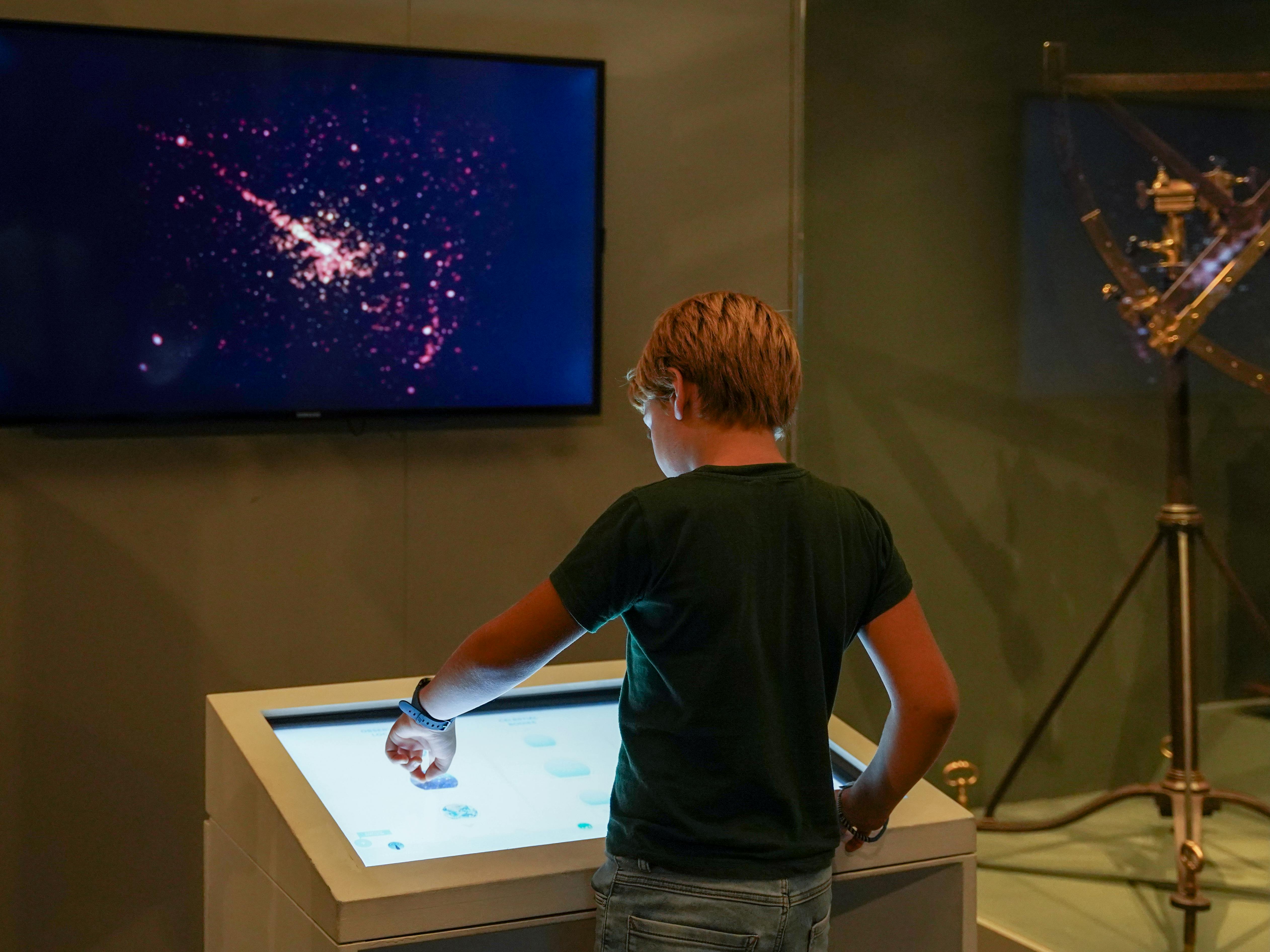 Milano, Museo della Scienza e della Tecnologia Leonardo da Vinci. Esposizione permanente "Spazio". Milano, Museo della Scienza e della Tecnologia Leonardo da Vinci. Esposizione permanente "Spazio". Un bambino di spalle esplora su uno schermo delle immagini dello spazio, attraverso un tavolo interattivo digitale.