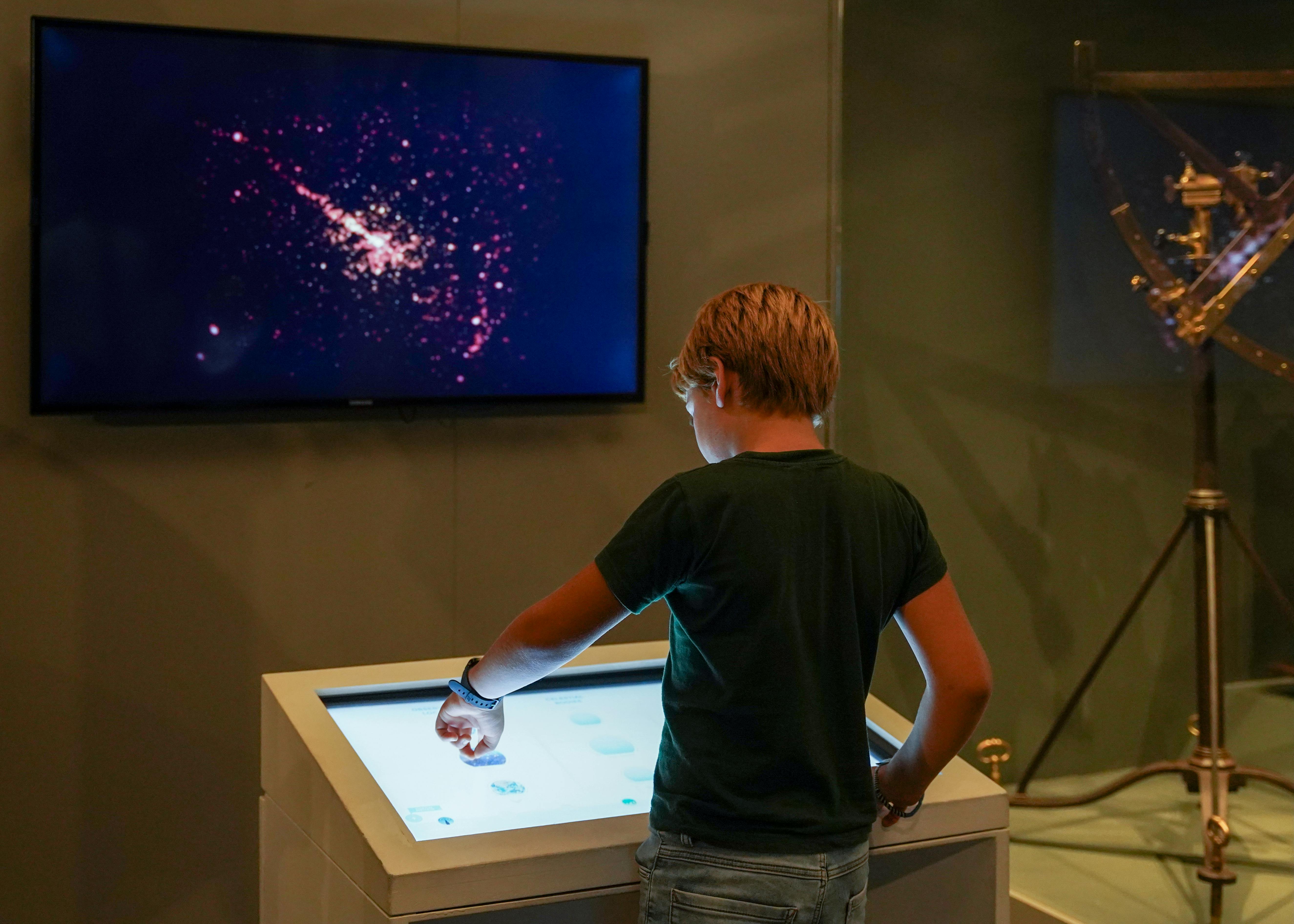 Milano, Museo della Scienza e della Tecnologia Leonardo da Vinci. Esposizione permanente "Spazio". Milano, Museo della Scienza e della Tecnologia Leonardo da Vinci. Esposizione permanente "Spazio". Un bambino di spalle esplora su uno schermo delle immagini dello spazio, attraverso un tavolo interattivo digitale.