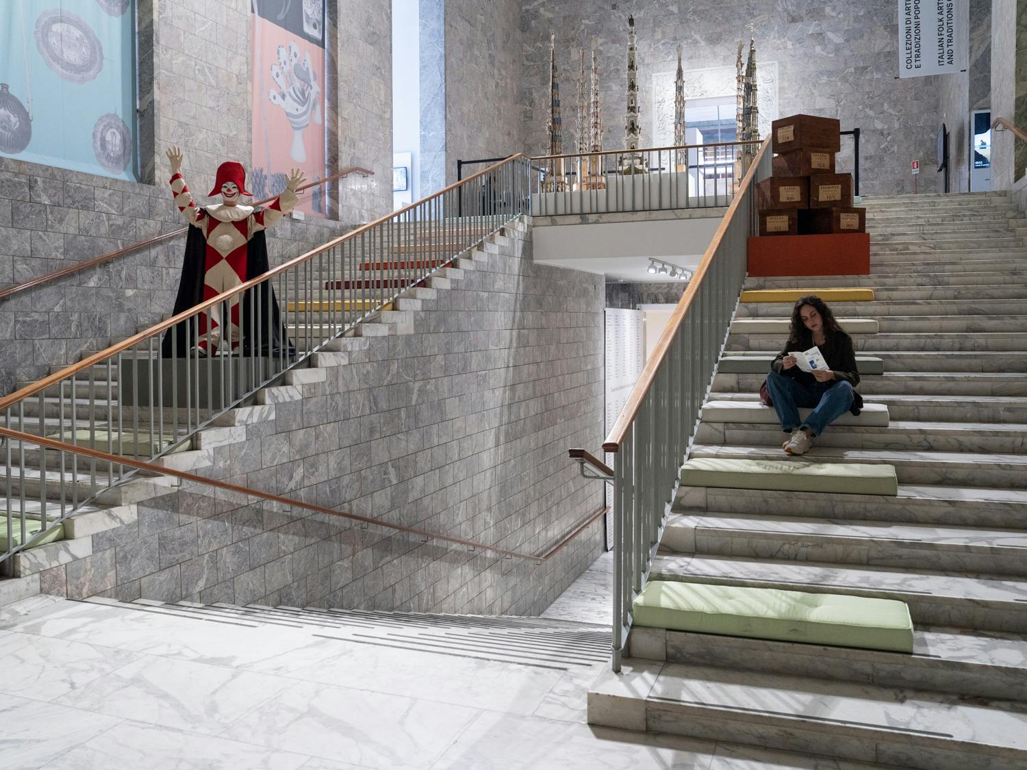 Roma, MUCIV, Museo delle Civiltà. Mostra "Le fiabe sono vere". Roma, MUCIV, Museo delle Civiltà. Allestimento della mostra "Le fiabe sono vere". Scalone di accesso al primo piano, con ragazza seduta e una maschera di Carnevale.