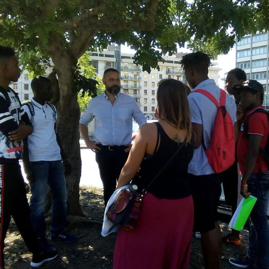 Riconoscersi sotto un albero di carrubo Sotto un albero di carrubo, in un'aiuola urbana, alcune persone di diverse provenienze condividono memorie legate all'albero di carrubo.