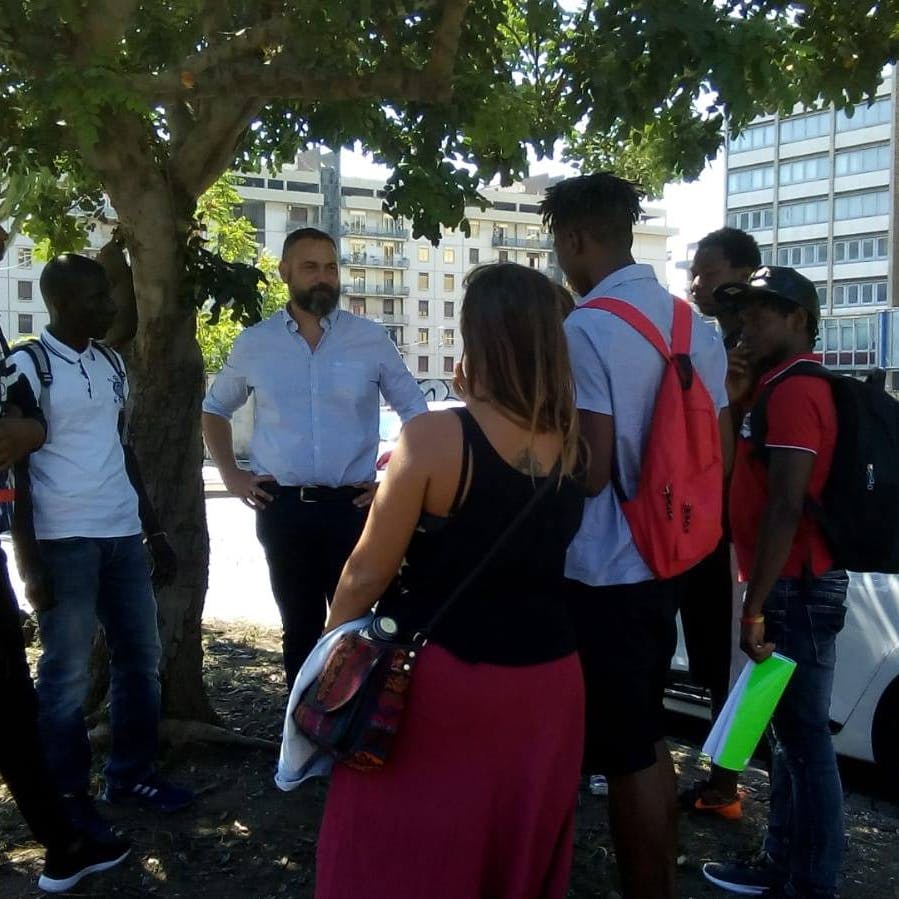 Meeting under a carob tree Under a carob tree, in an urban flowerbed, several people from different backgrounds share memories connected to the carob tree