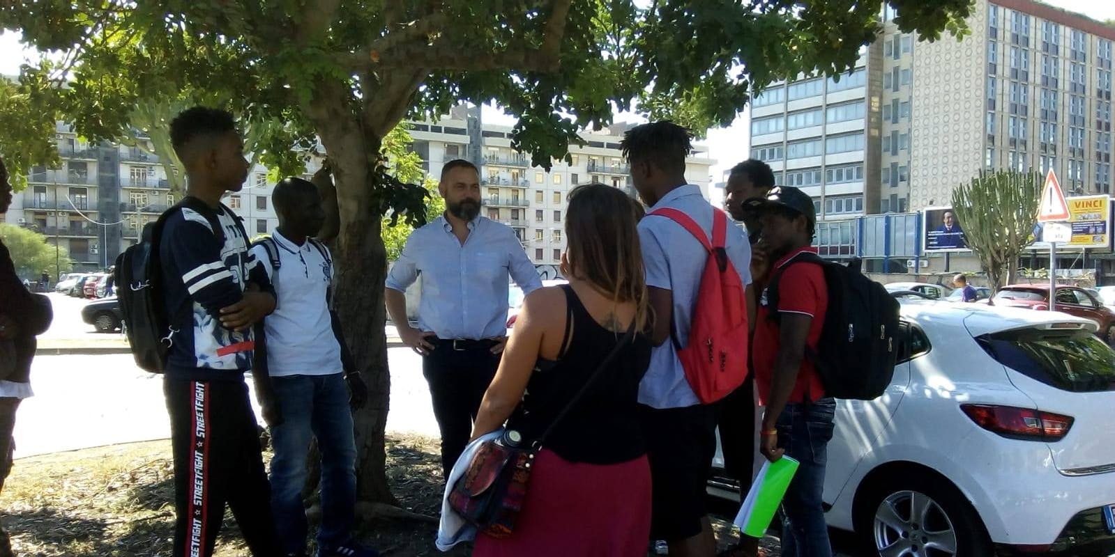 Riconoscersi sotto un albero di carrubo Sotto un albero di carrubo, in un'aiuola urbana, alcune persone di diverse provenienze condividono memorie legate all'albero di carrubo.