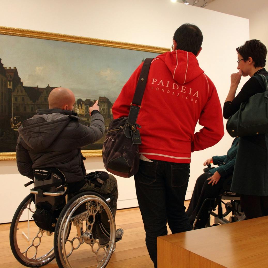Physical and relational accessibility in the museums A group of visitors observes a work in a museum: the presence of people in wheelchairs and a staff member highlights how cultural accessibility involves not only space, but also the quality of relationships, guidance, and communication