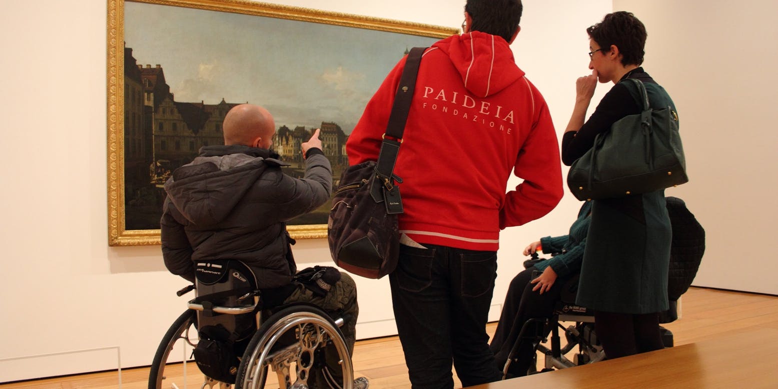 Physical and relational accessibility in the museums A group of visitors observes a work in a museum: the presence of people in wheelchairs and a staff member highlights how cultural accessibility involves not only space, but also the quality of relationships, guidance, and communication