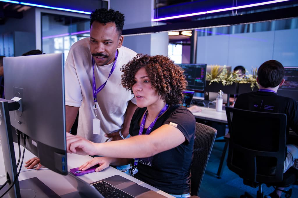 A man and a woman work at a computer in the office, with the woman typing in front of the monitor.