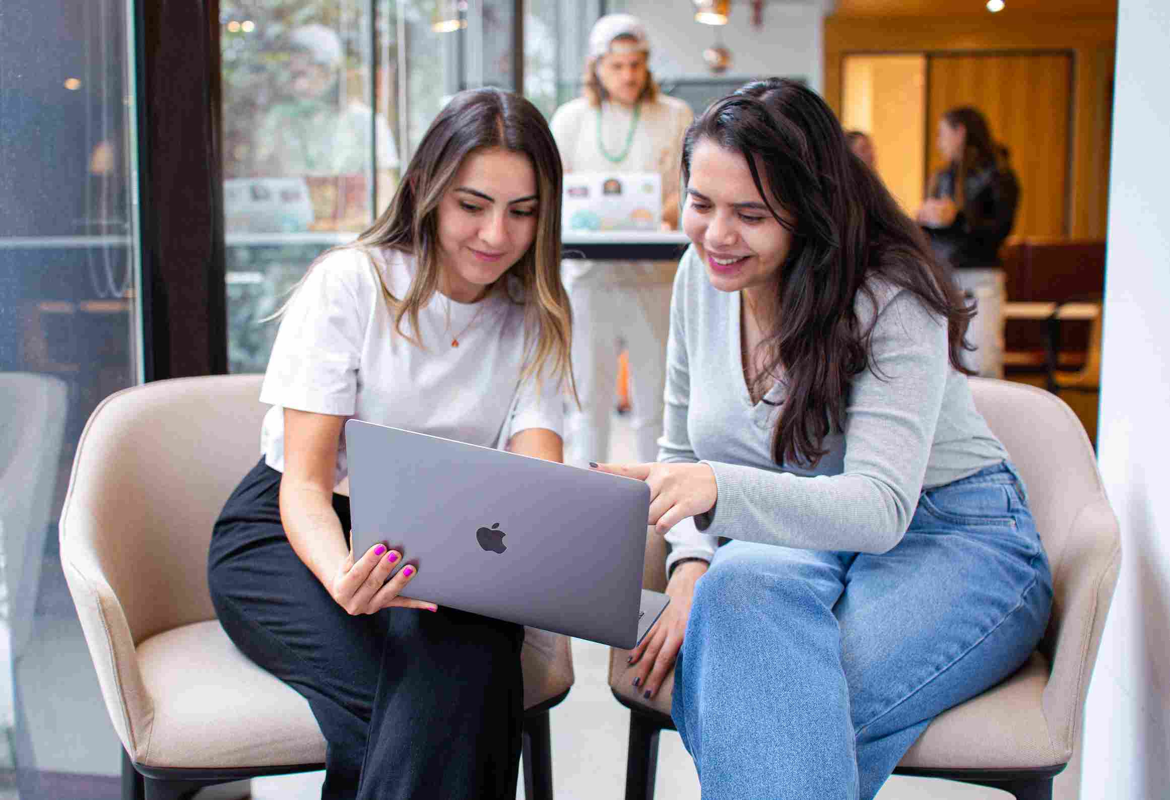 Two smiling women sharing ideas over a laptop screen.