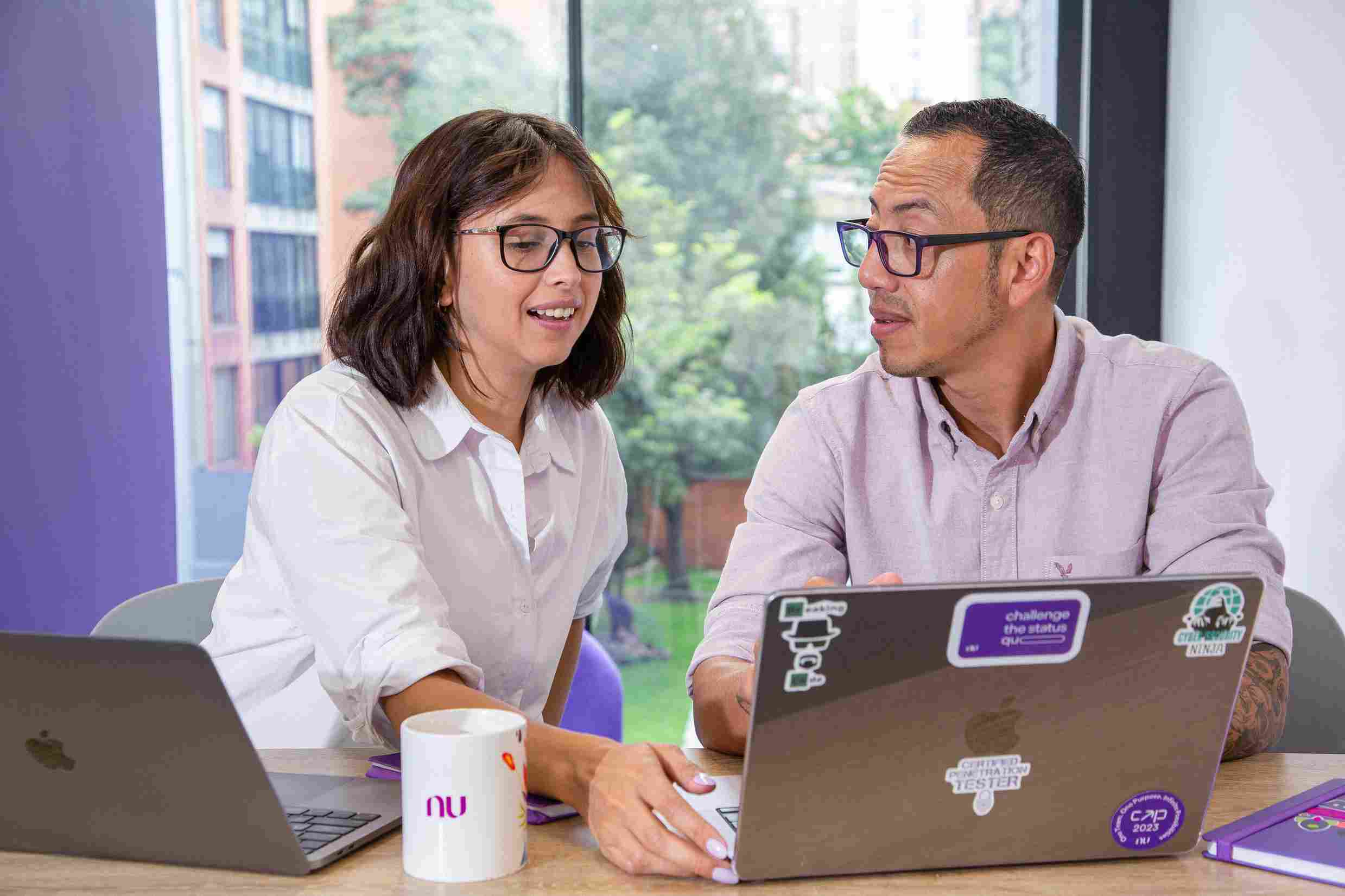 Un hombre y una mujer dialogan frente a sus laptops en la mesa.