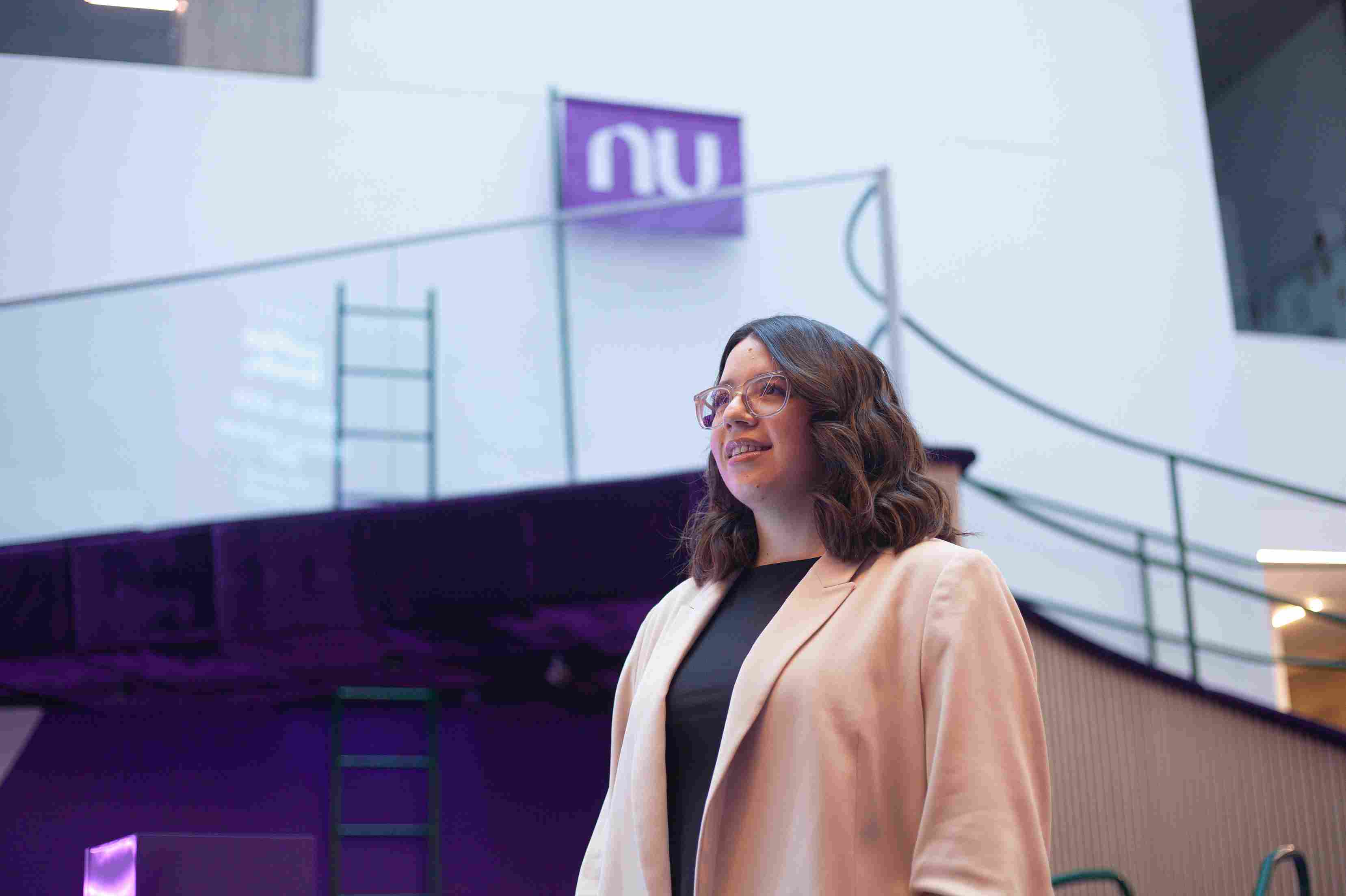 Woman in a blazer smiling on a modern office walkway.