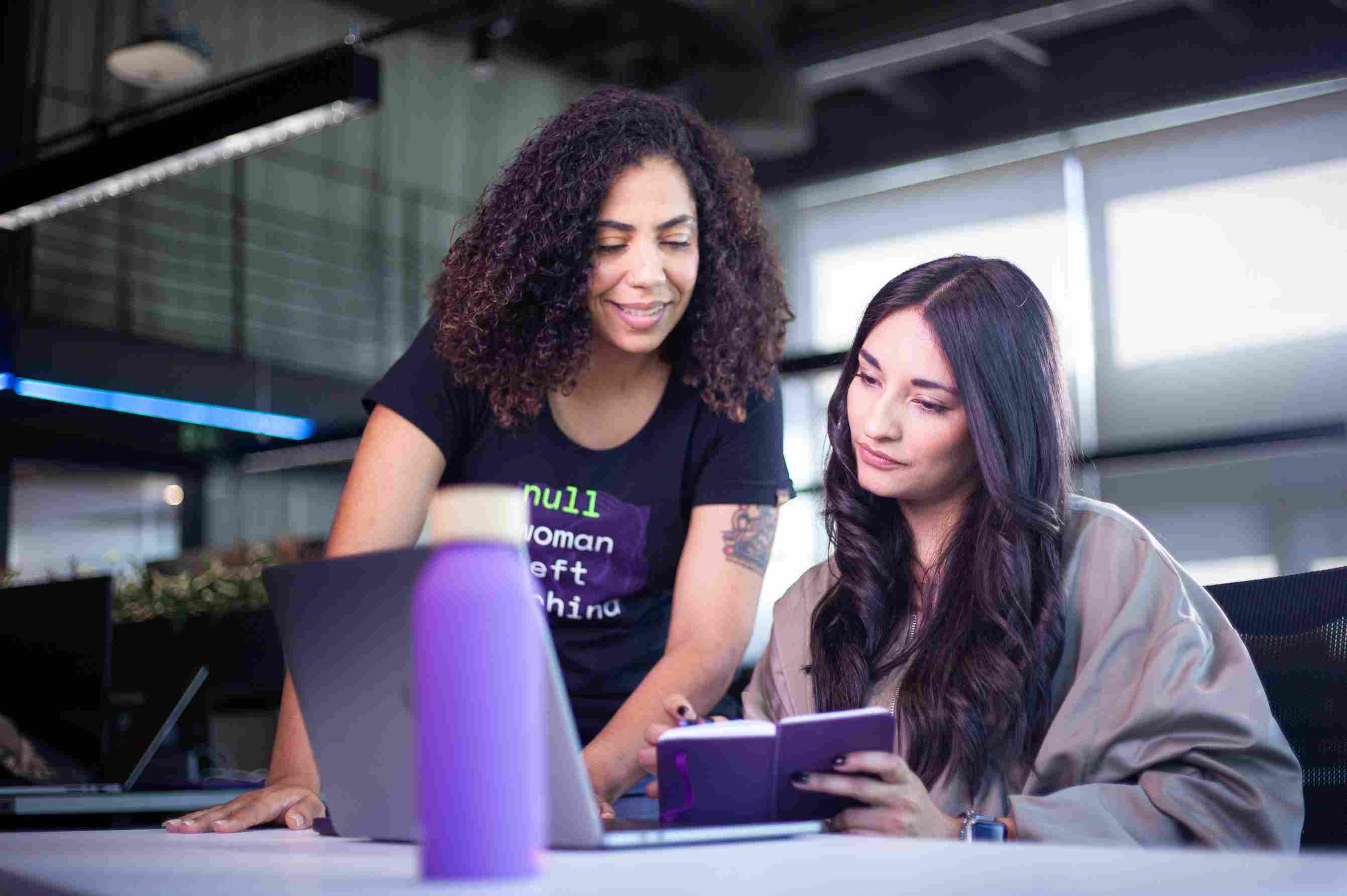 Two women reviewing notes and looking at a laptop screen.