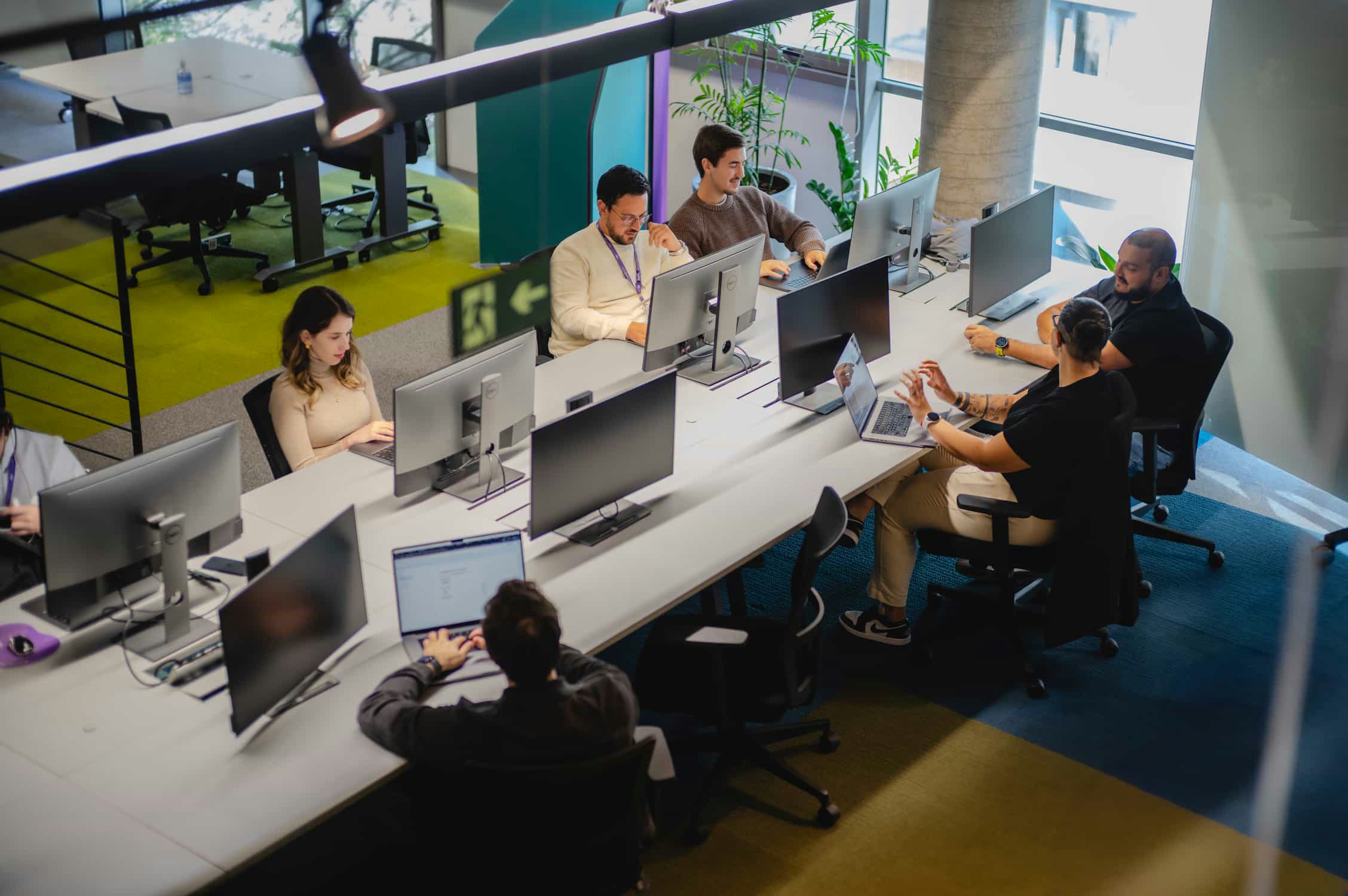Siete personas trabajando en una mesa de oficina compartida y con espacio para una persona más