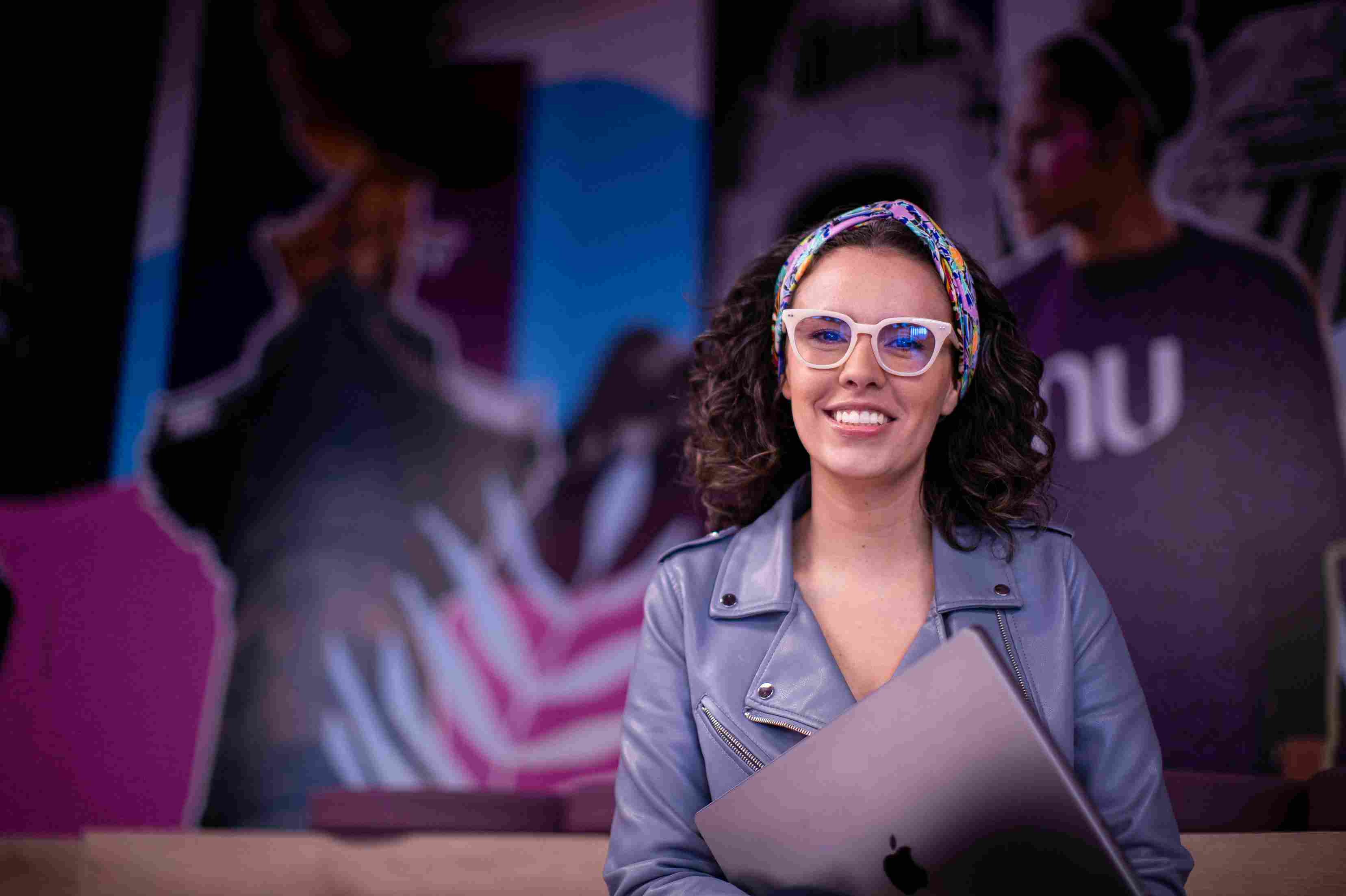 Smiling woman wearing glasses and holding a closed laptop.