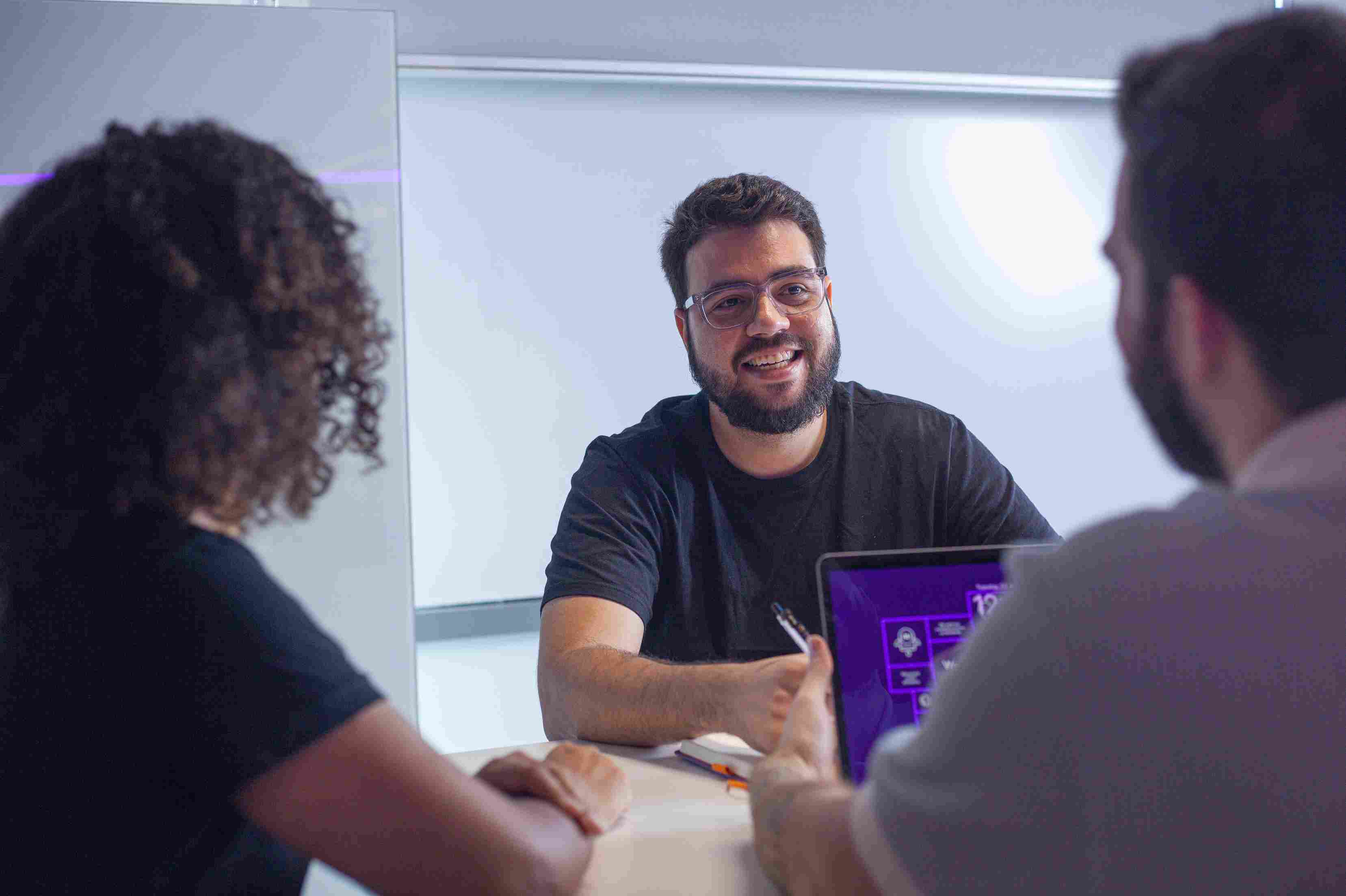 Man with glasses smiling during a meeting with colleagues.