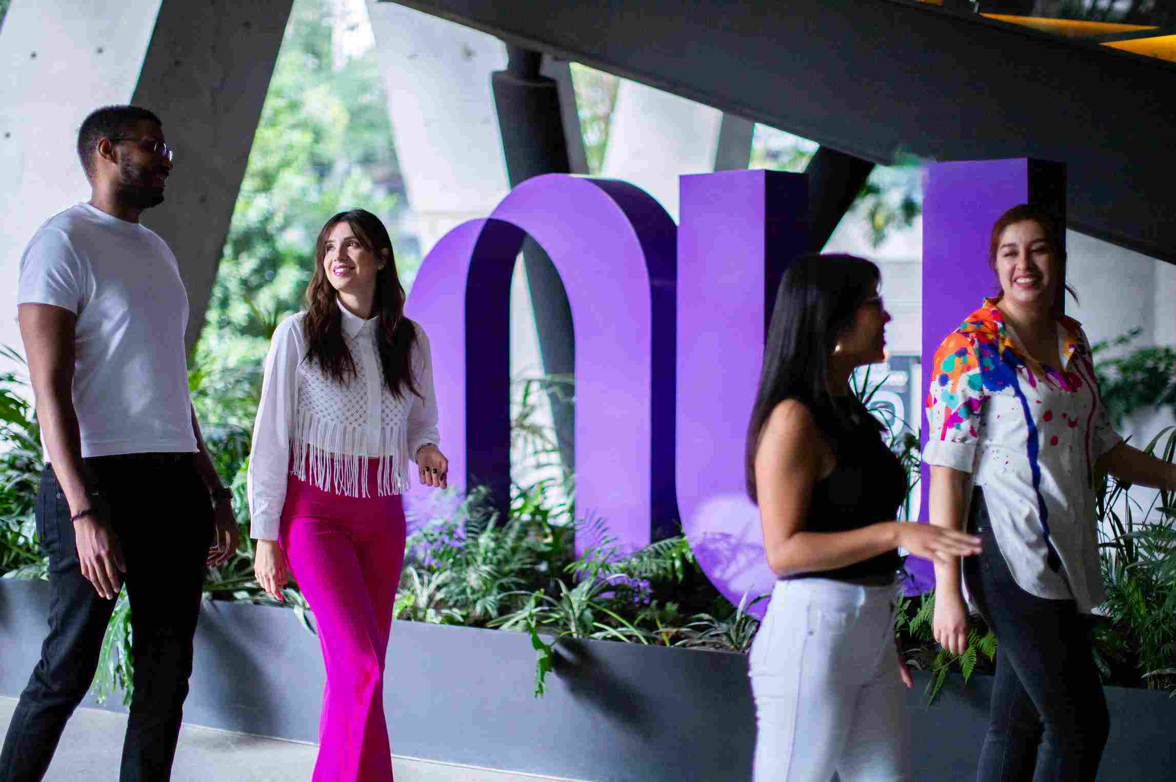 People chatting while walking by a large purple Nu sign.