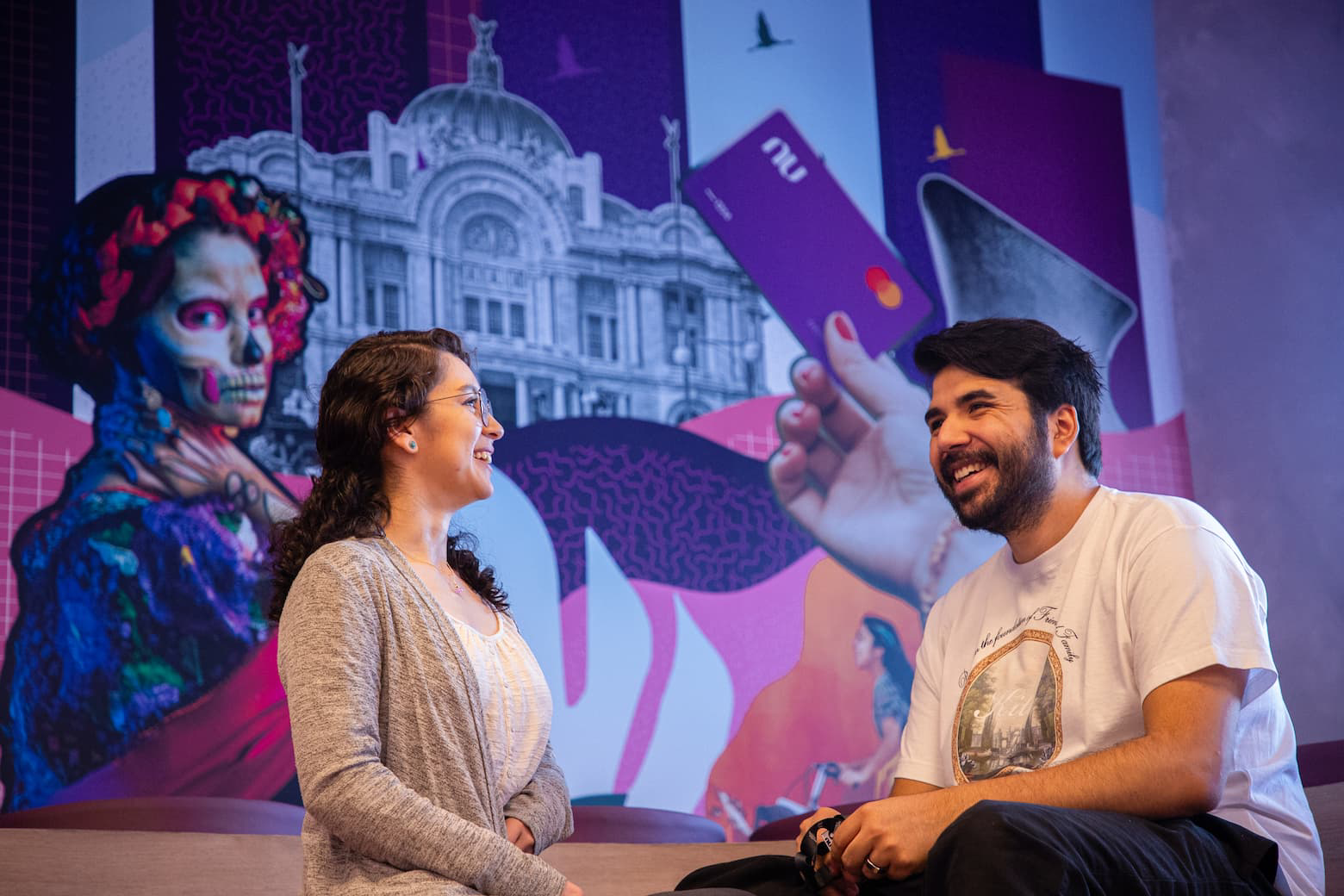 Two people chat in an office space with purple artwork in the background.
