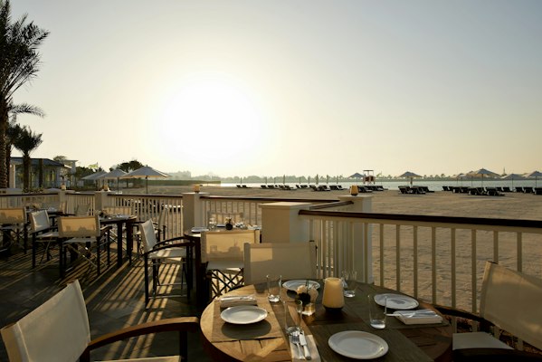 Beachfront dining area with tables set for a sunset view.