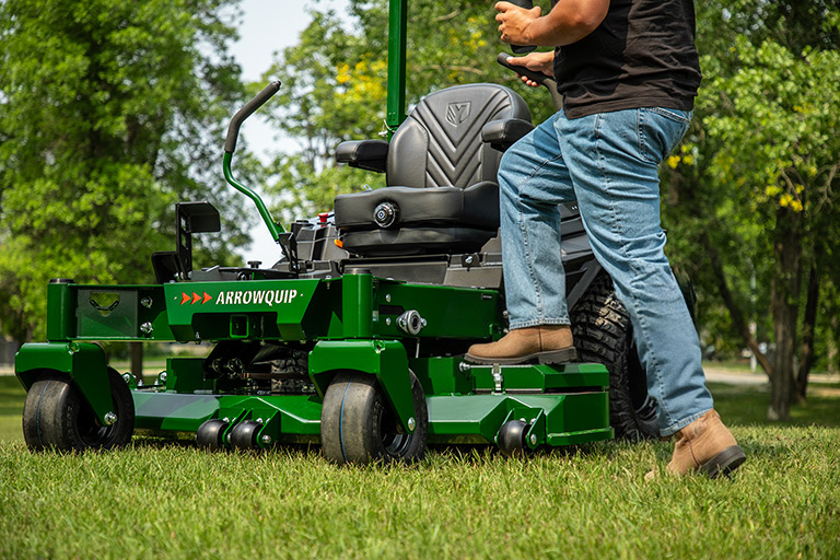 Man stepping on deck of Arrowquip 720 commercial zero-turn mower outdoors, designed for power and precision mowing