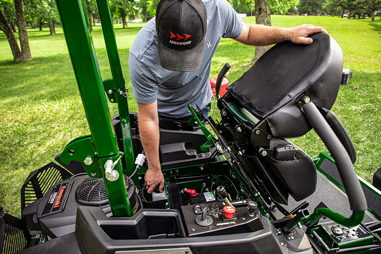Man performing maintenance on Arrowquip Mowers zero-turn mower designed for durability and easy service.