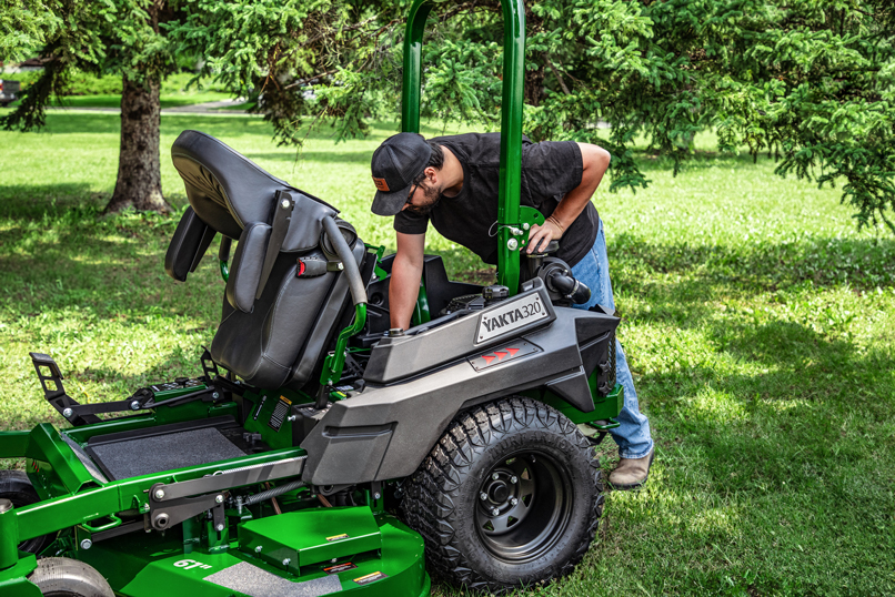 Man checking Yakta 320 zero-turn mower with reinforced steel deck and durable design