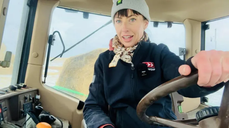 Erin Galloway from Our Wyoming Life driving a tractor hauling hay to feed cattle in her Arrowquip jacket