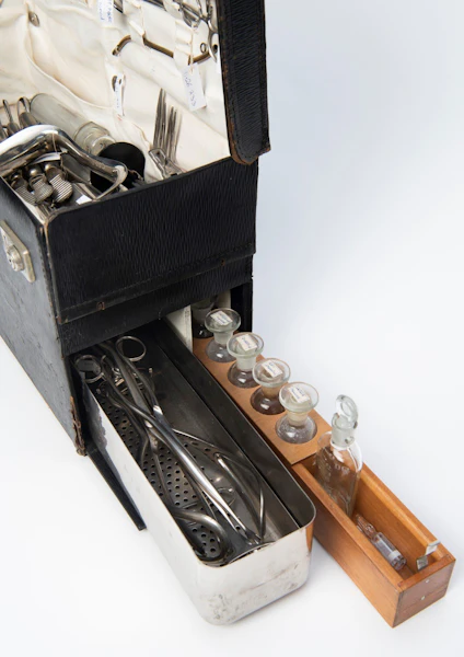 Detail of home birth kit showing a metal tray and wooden tray partly slid out of the base of the black case.