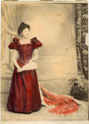A young woman in a full length gown with a train, also holding a fan